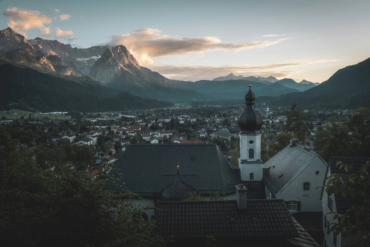 View over Garmisch-Partenkirchen towards the Wetterstein mountains at dusk, a church with an onion dome in front