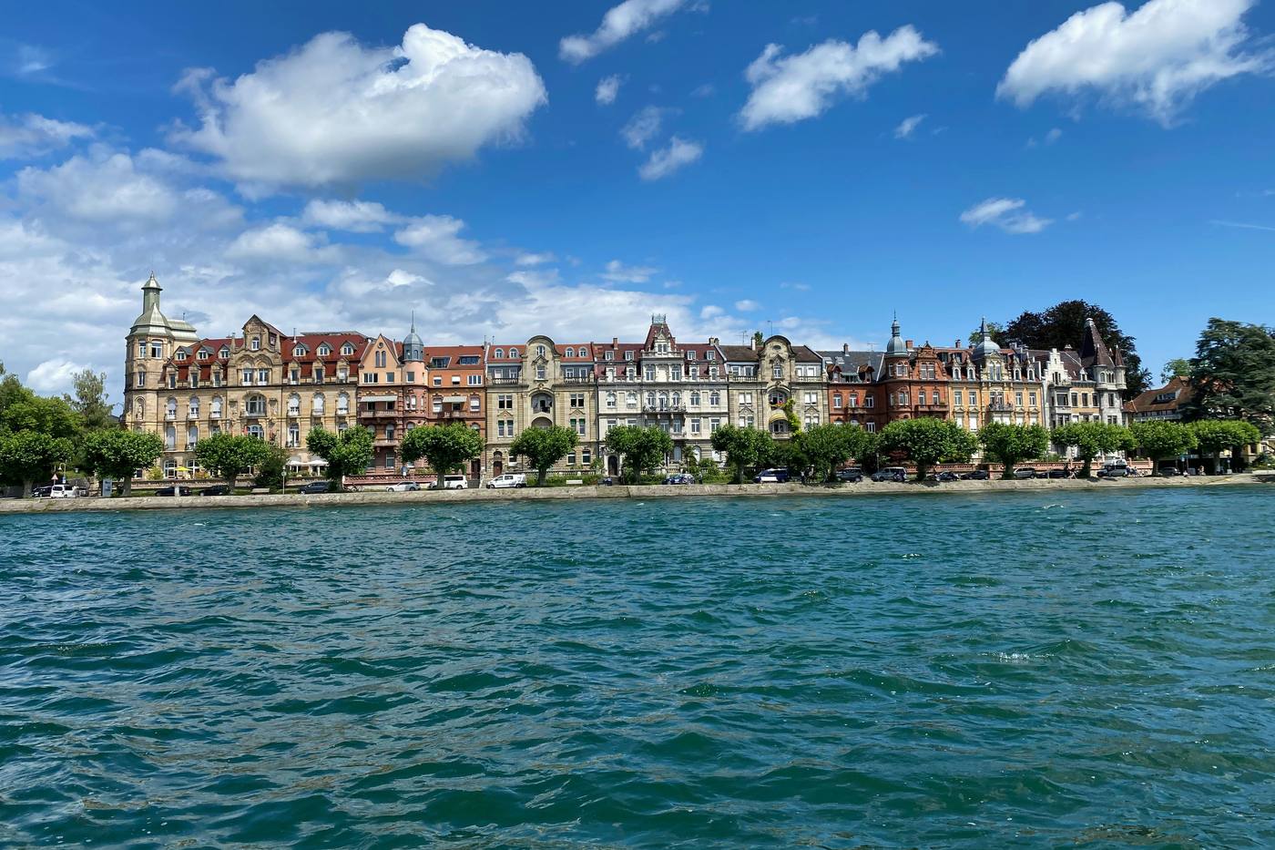 A row of ornate 19th-century houses on the Konstanz shore under a blue sky, seen from the water