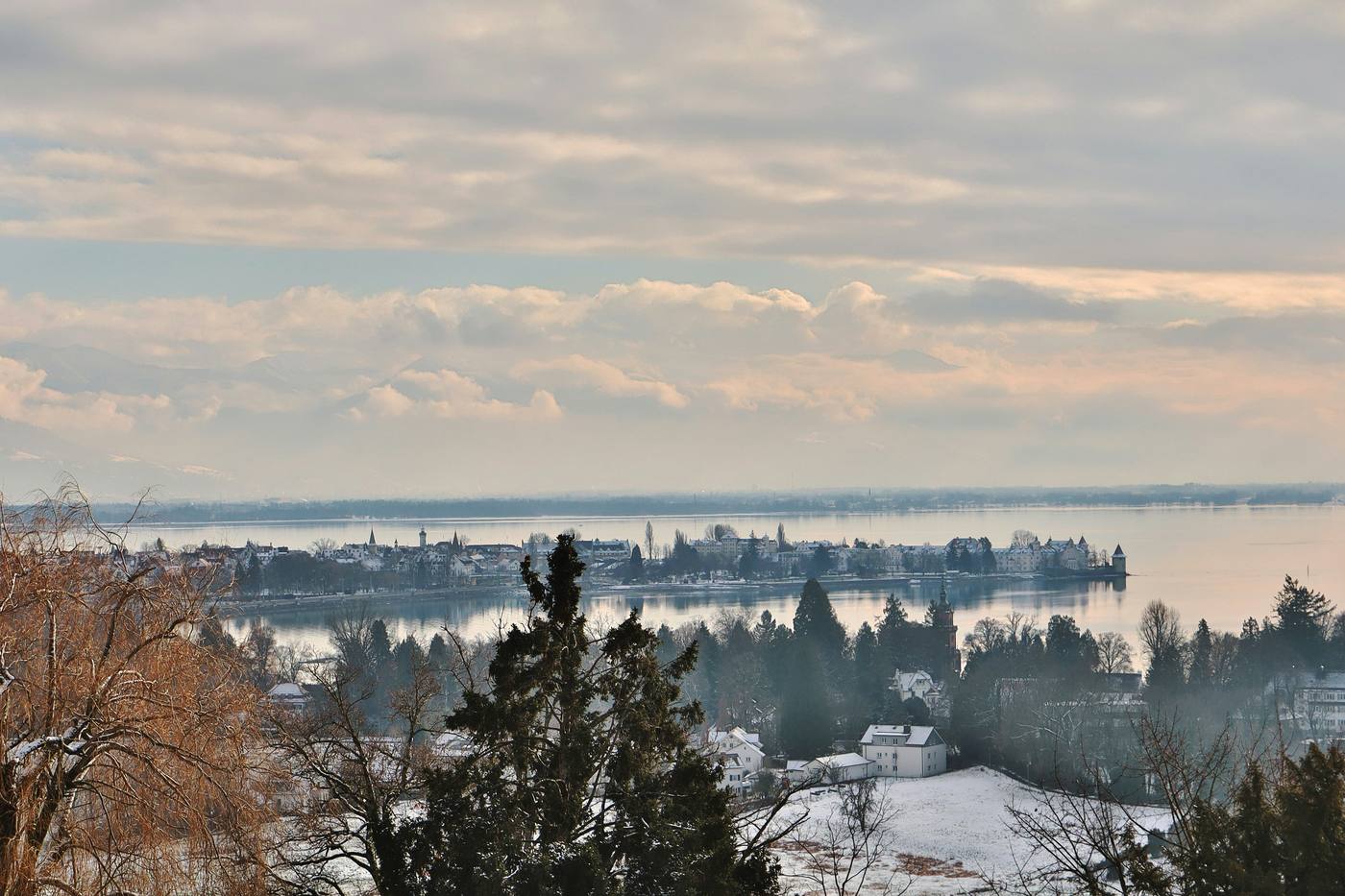 Lindau’s island old town in winter, seen from snowy hills on the mainland, the lake and the Alps behind