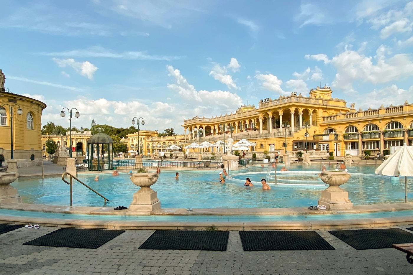 Outdoor thermal pools in front of a yellow neo-baroque bath building